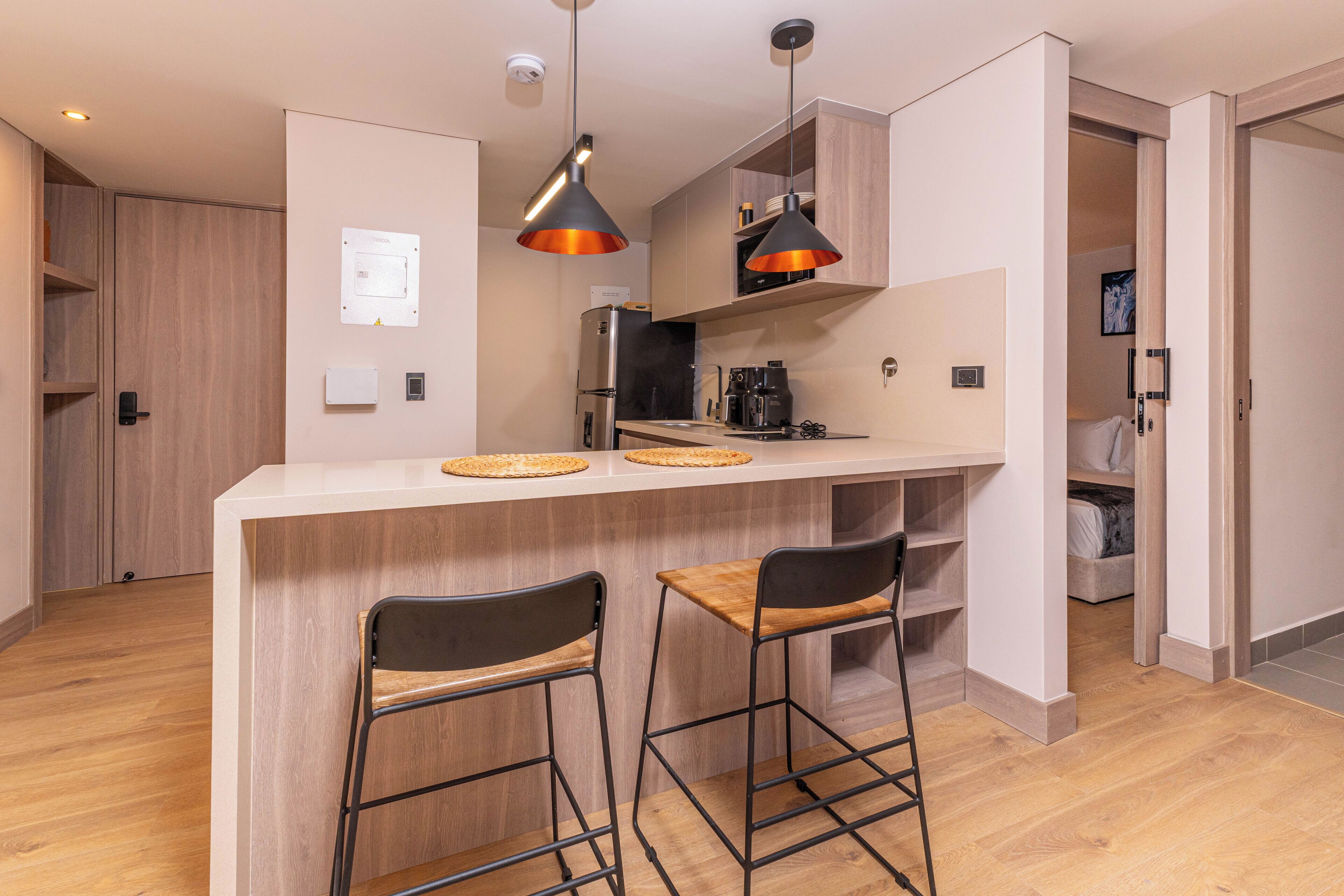 A modern kitchen with a central island, two bar stools, pendant lighting, and a built-in refrigerator.