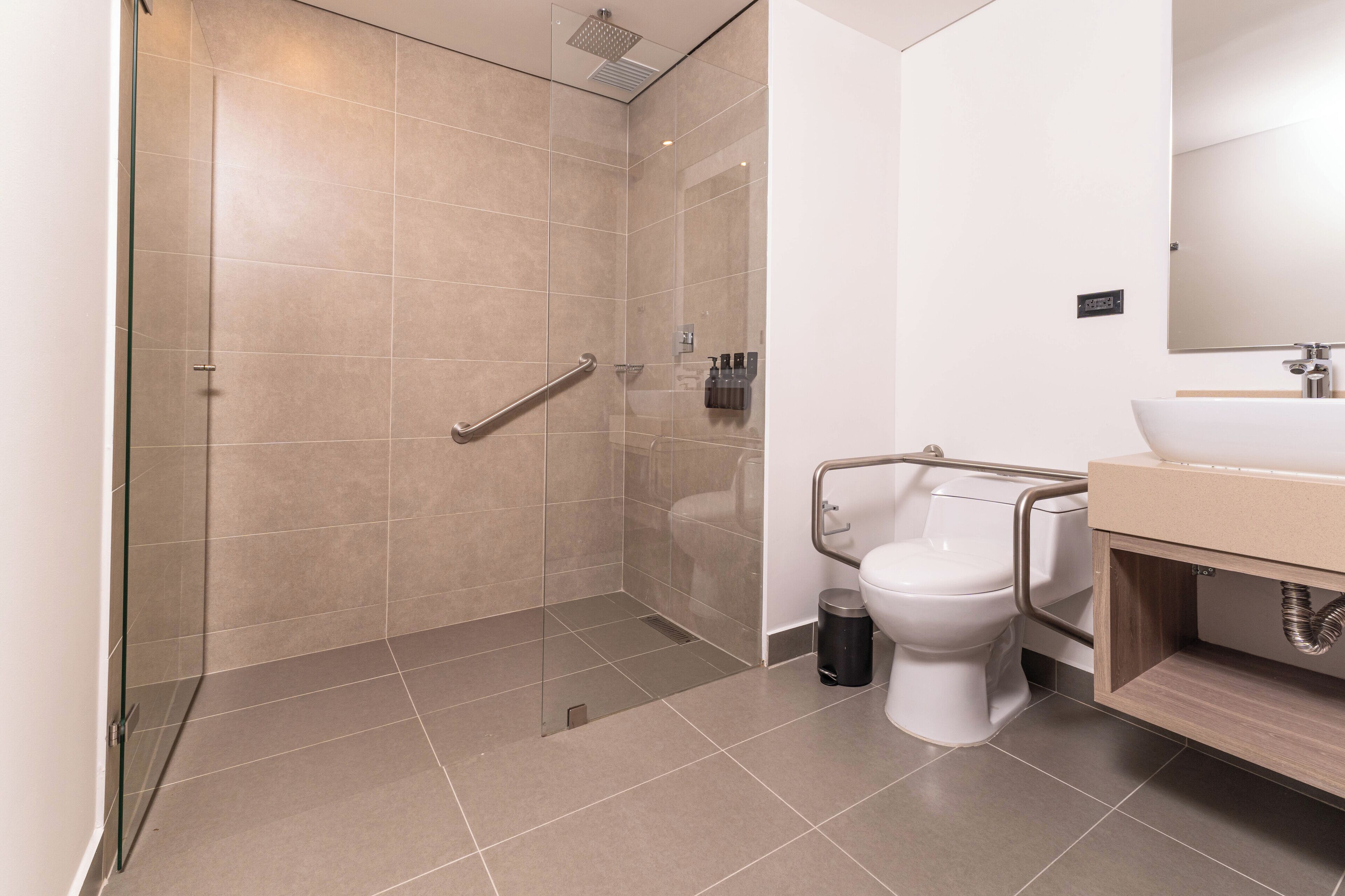 Une salle de bain moderne avec une douche à parois de verre, des toilettes blanches et un lavabo avec un meuble-vasque en bois.