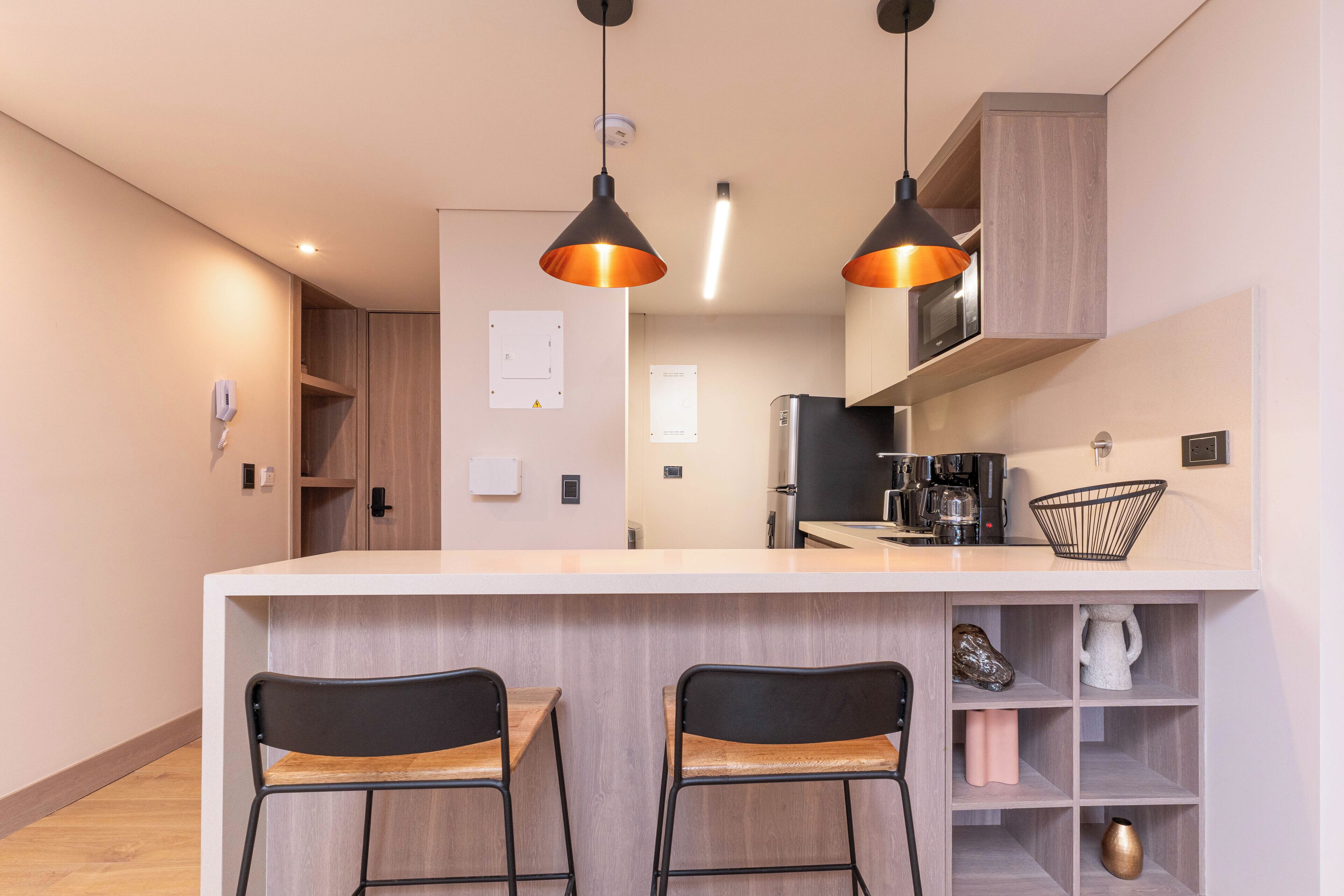 Una cocina moderna con dos taburetes de bar, iluminación colgante, microondas y cafetera.