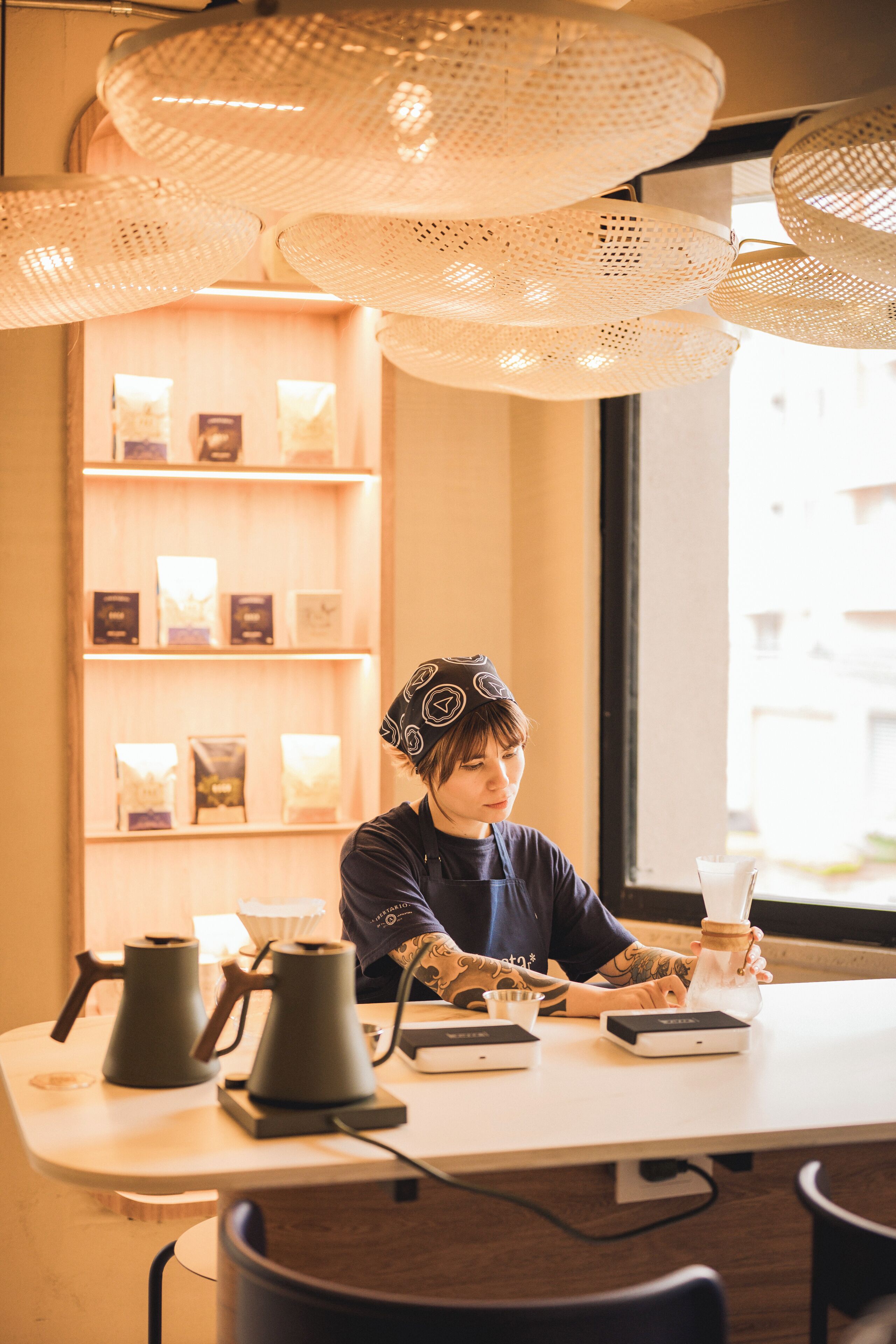 Une personne assise à une table, devant une machine à café, une balance et un verre de lait.