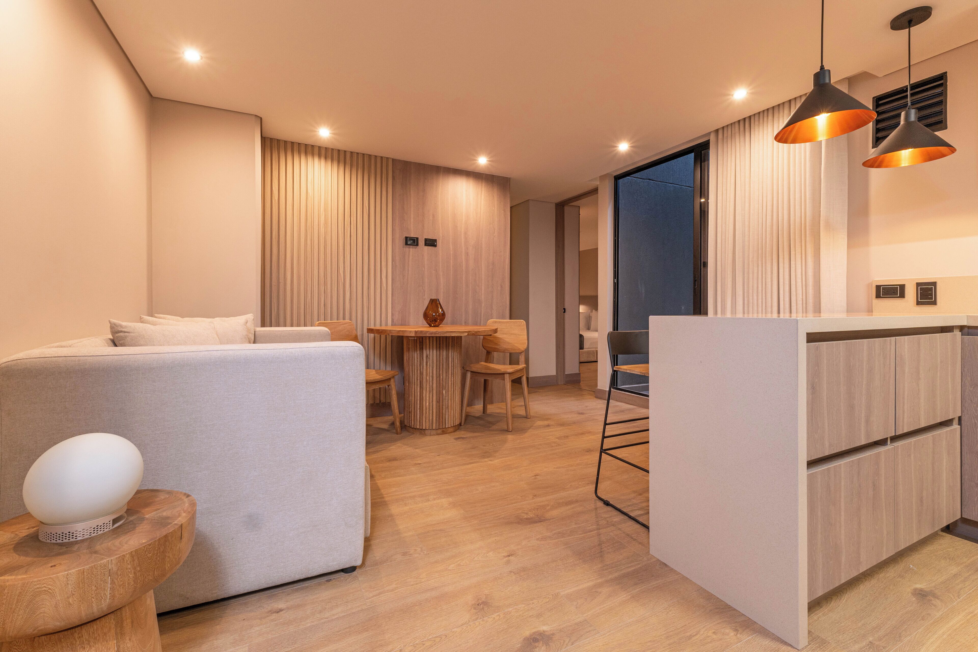 A modern living room with a sofa, a round wooden table, and a kitchen area with a countertop and cabinets.