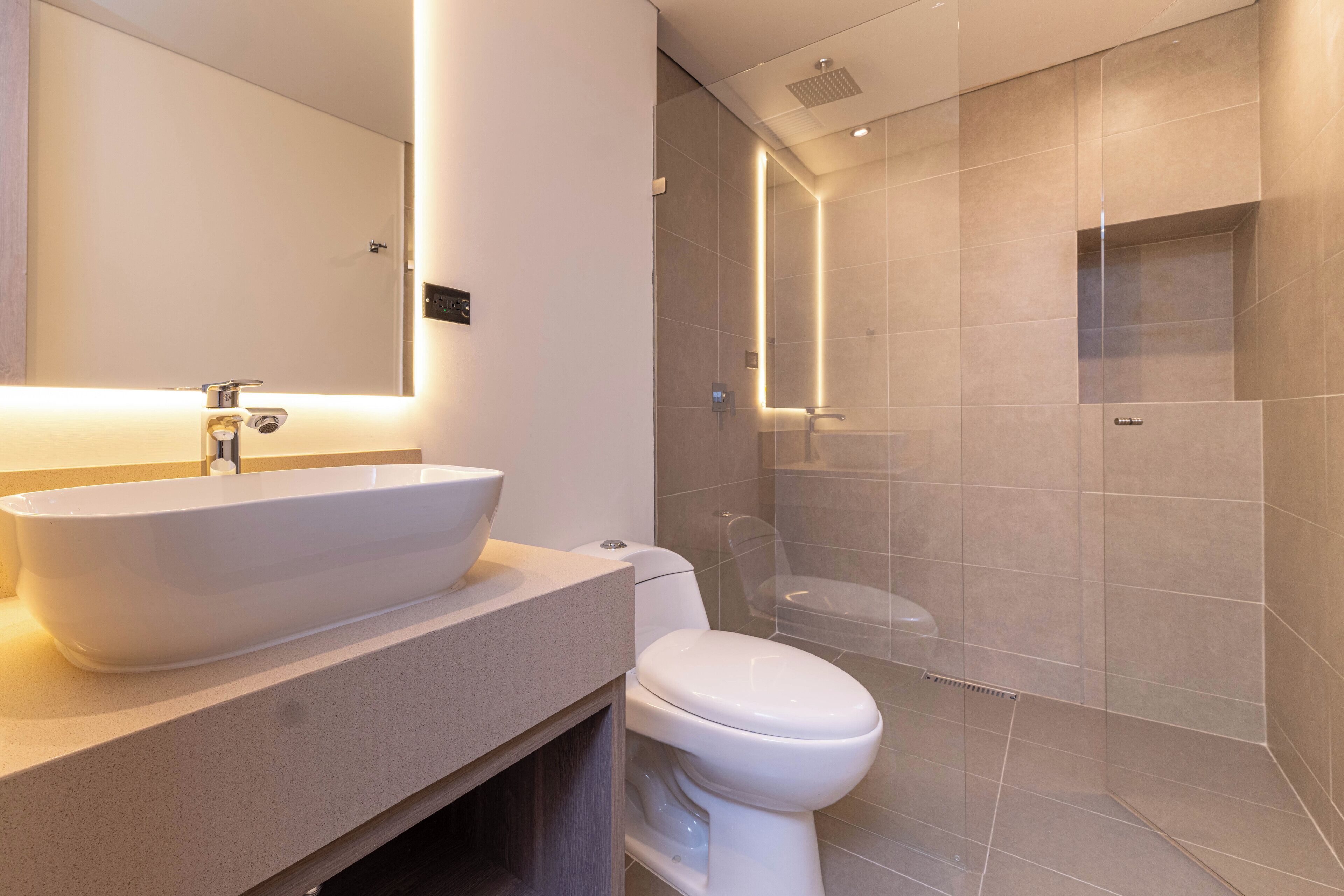 A modern bathroom with a large white sink, a toilet, and a glass-enclosed shower area.