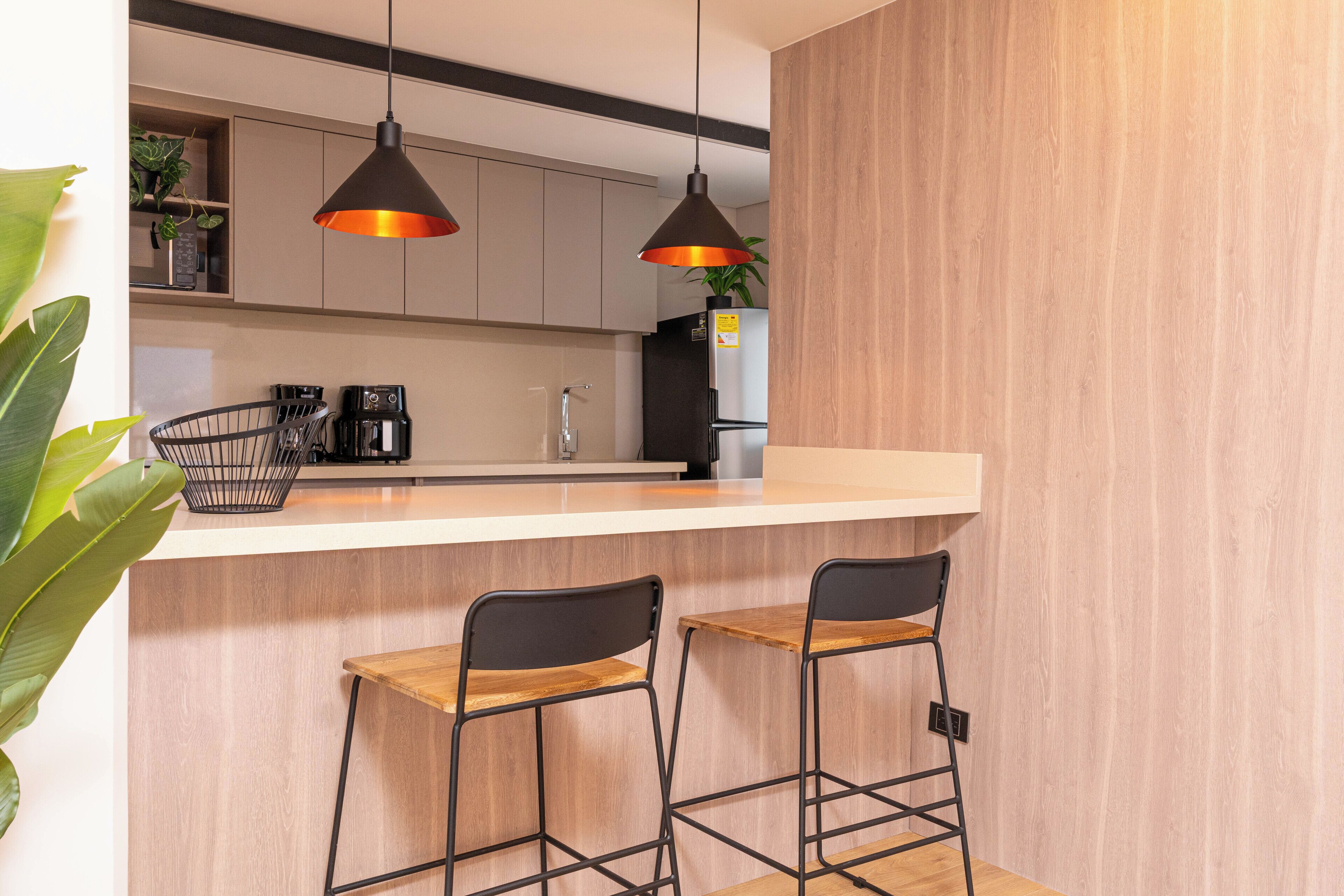 A modern kitchen with a wooden countertop, two black metal chairs, and pendant lights.