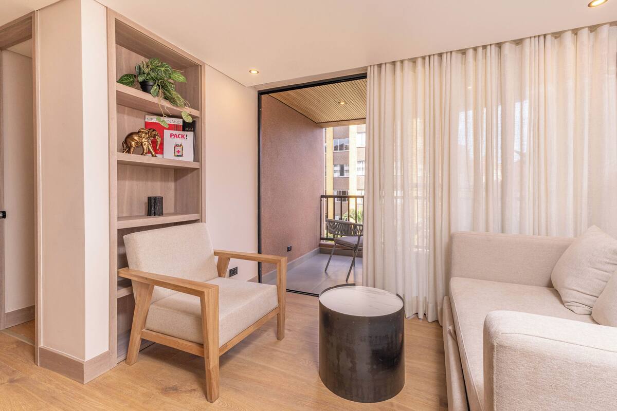 Un salon moderne comprenant un canapé, un fauteuil, une petite table et une bibliothèque agrémentée d’objets décoratifs.