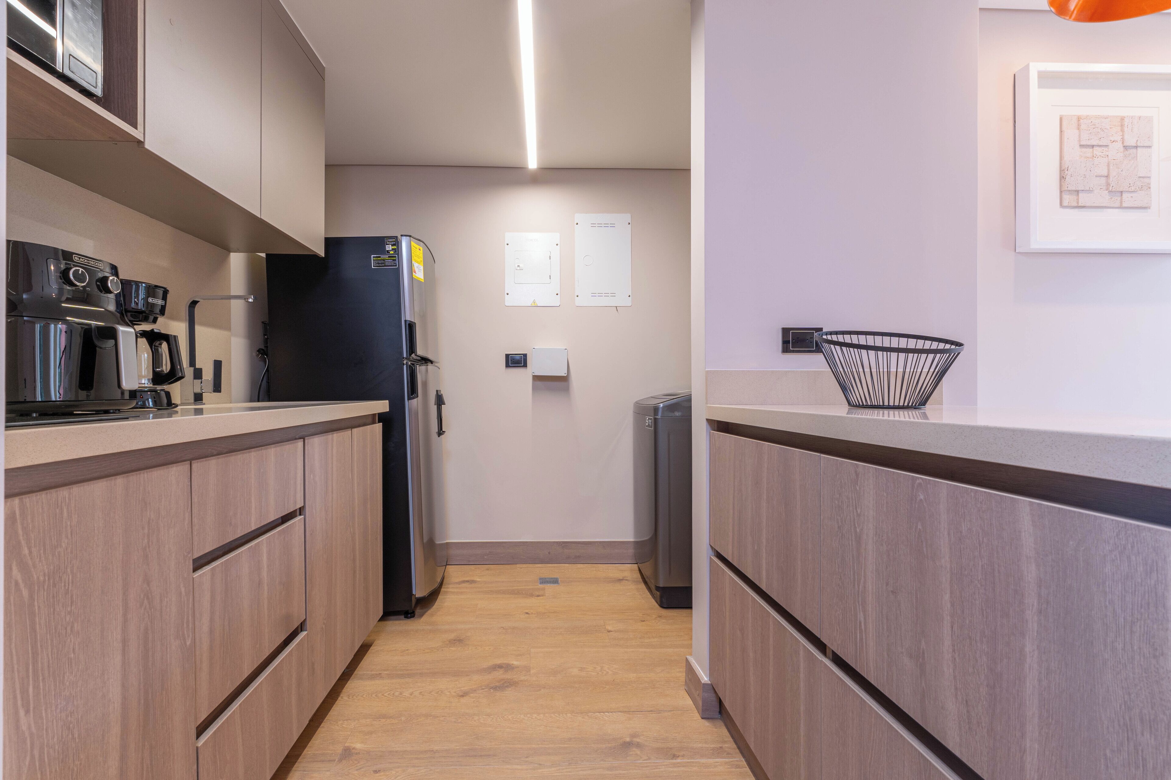 Una cocina moderna con armarios de madera, un refrigerador negro, una cafetera y un cubo de basura.