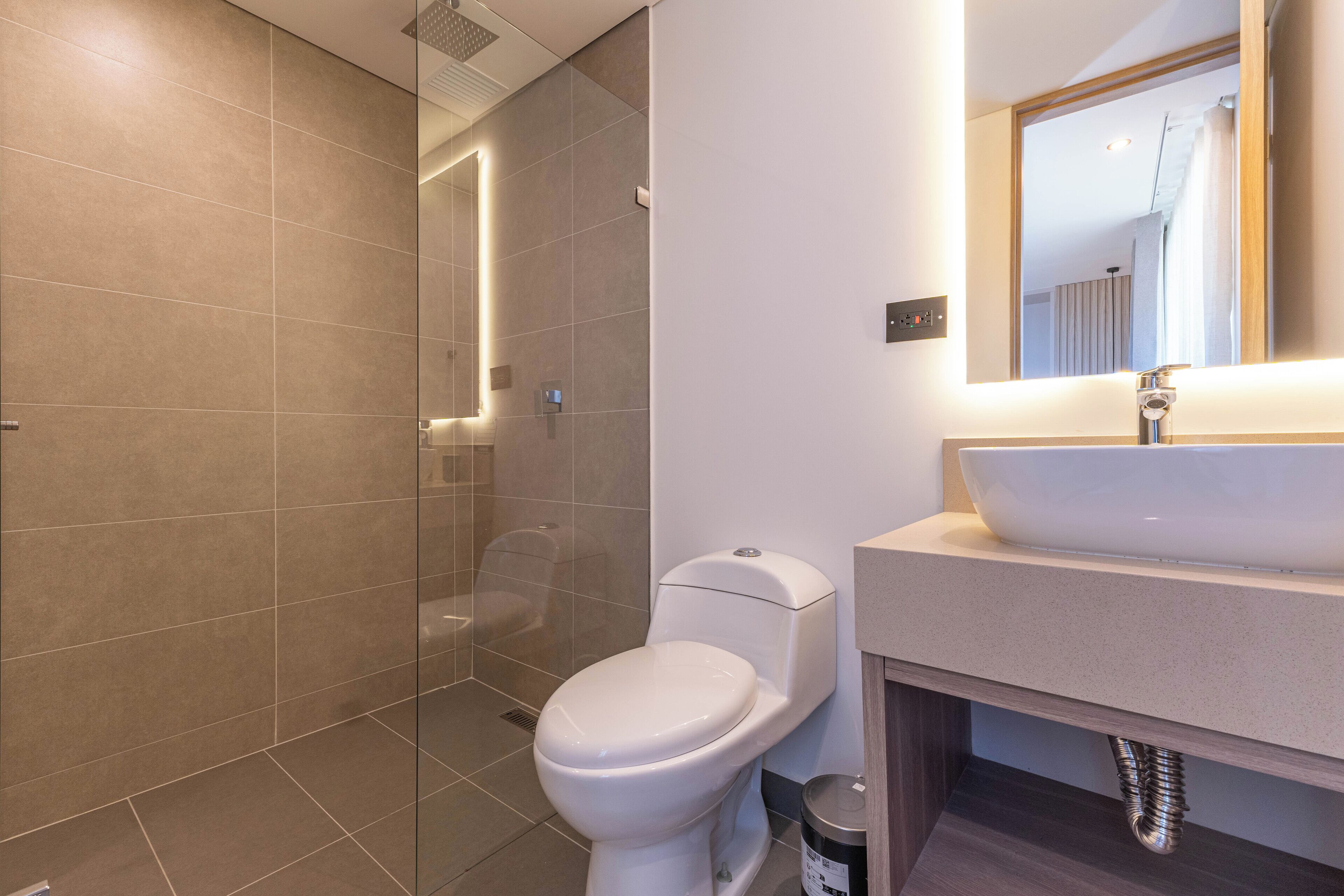 A modern bathroom with a glass-enclosed shower, a white toilet, and a sink with a mirror above it.