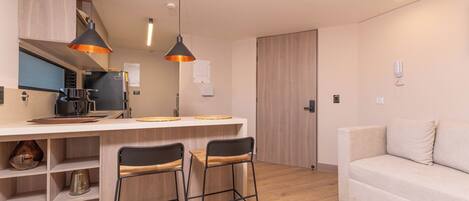 Een moderne keuken met een centraal eiland, twee barkrukken, een bank en hanglampen.