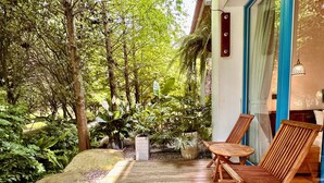 Een houten terras met stoelen, omgeven door weelderige begroeiing en een grote rots.