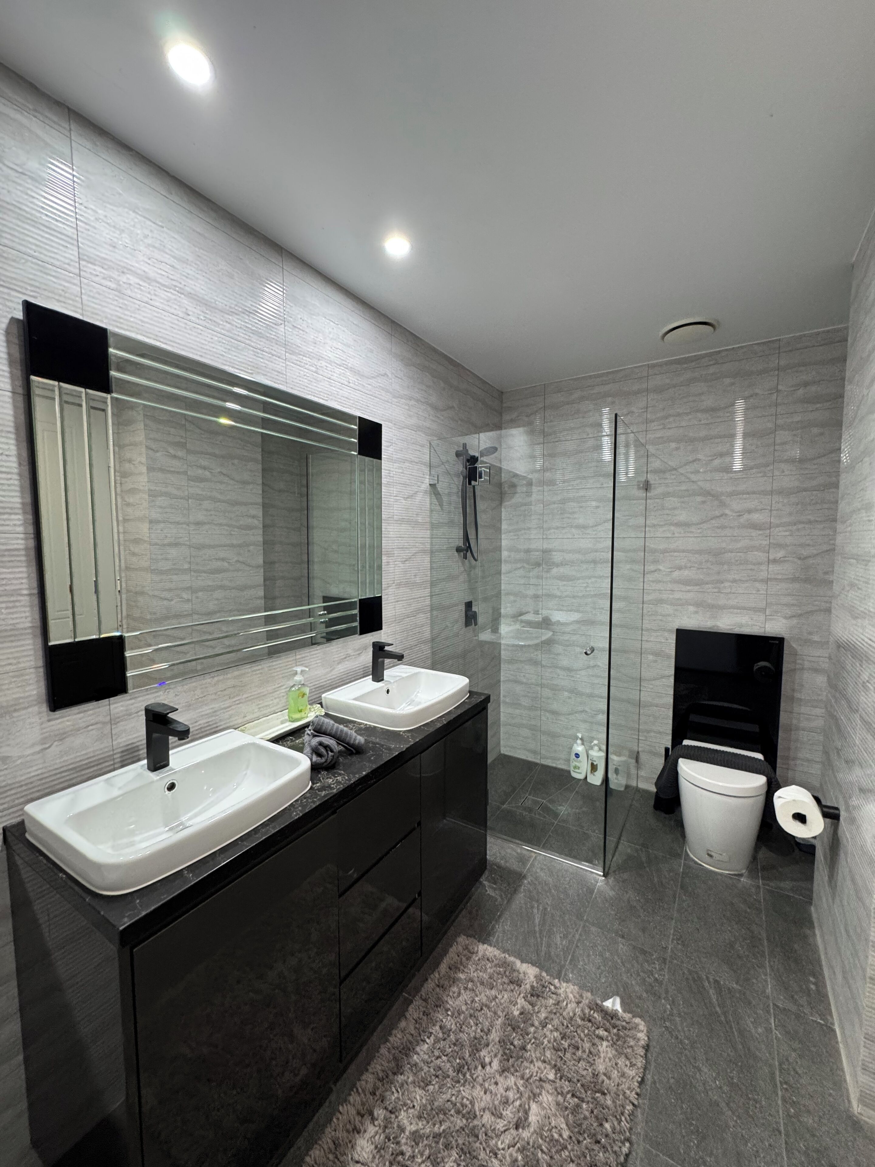A modern bathroom with two sinks, a glass shower enclosure, and a toilet.