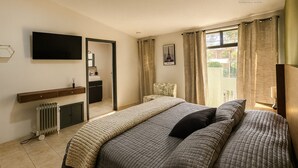 A bedroom with a bed, a TV, a bathroom, and a view of the outside.