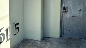 A building entrance with a light green wall, a door with a metal handle, and a small light fixture above the door.