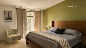 A bedroom with a bed, a nightstand, a chair, and a window with curtains.