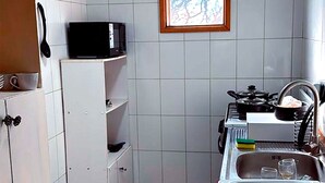Pieni keittiö, jossa on valkoiset kaapit, mikroaaltouuni, liesi ja ikkuna, josta avautuu näkymä puihin.