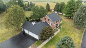 Une maison à deux étages avec un garage, entourée d’arbres et d’une cour gazonnée.