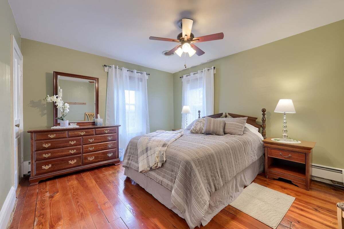 Een slaapkamer met een bed, een dressoir, een nachtkastje en een plafondventilator.
