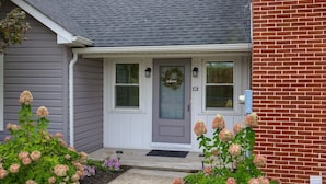 A house with a grey door, a brick wall, and a porch with hydrangea plants. - Historic Gettysburg Homestead for Large Groups (Gettysburg)