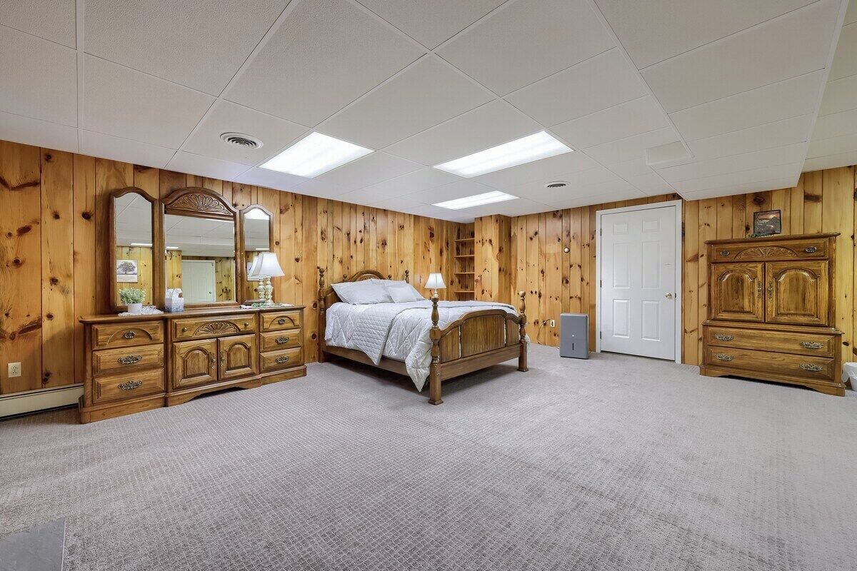 A bedroom with a wooden paneled wall, a bed with a headboard, a dresser, a mirror, and a door.