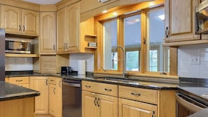 A kitchen with wooden cabinets, a stainless steel dishwasher, a coffee maker, and a window with a view. - Historic Gettysburg Homestead for Large Groups (Gettysburg)