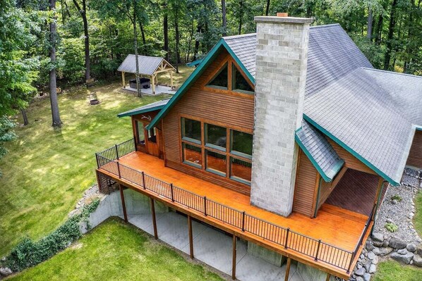 Eine moderne Blockhütte mit einer großen Veranda, einem Steinsschornstein und einer umliegenden Waldlandschaft.