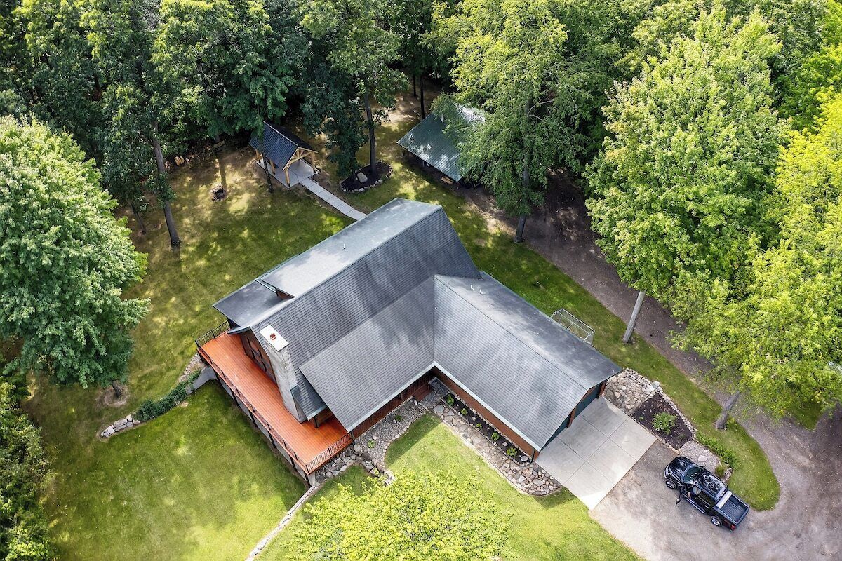An aerial view of a modern house with a sloped roof, surrounded by lush greenery and a well-maintained lawn.