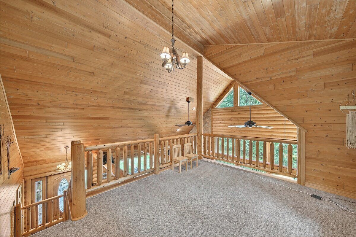 Une pièce spacieuse aux murs et au plafond en bois, un balcon doté d’une balustrade en bois et un lustre.