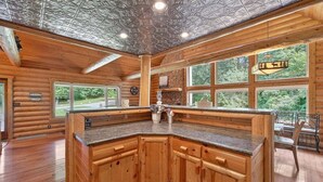 A log cabin interior with a kitchen island, large windows, and a ceiling with a geometric pattern. - Forest Escape w/ Hot Tub & Bunk Rooms (Sturgis)