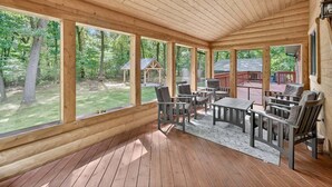A covered outdoor area with wooden flooring, large windows, and outdoor furniture. - Forest Escape w/ Hot Tub & Bunk Rooms (Sturgis)