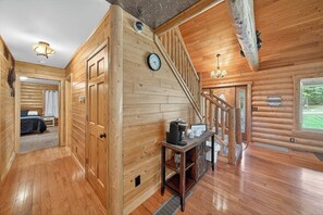 Ein Interieur einer Blockhütte mit einer Holztreppe, einer Uhr, einer Kaffeestation und Blick ins Freie.