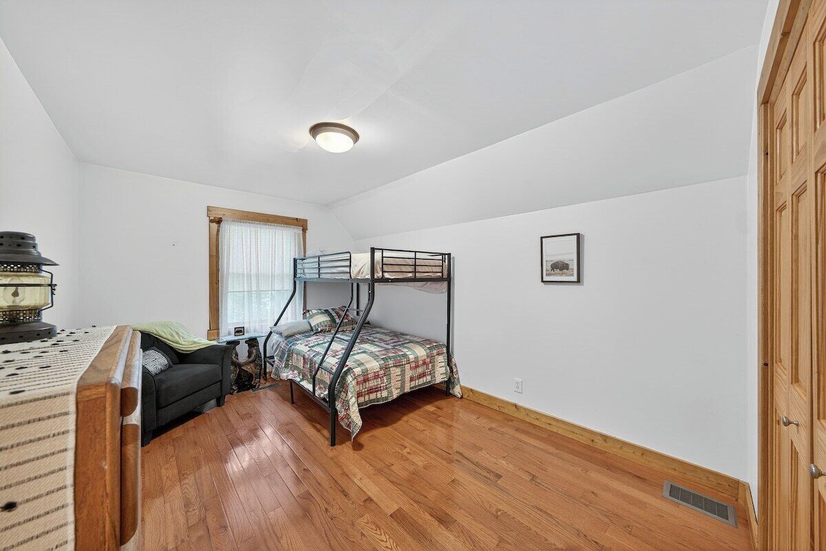 Une chambre avec un lit superposé, un bureau avec une lampe, une chaise et une fenêtre avec des rideaux.