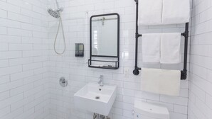 A bathroom with white tiled walls, a white sink, a mirror, a towel rack, and a showerhead. - King Room, Heart of Times Square (New York)