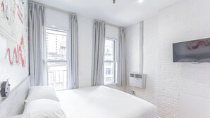 A modern hotel room with a large bed, two windows with curtains, a mounted TV, and a white brick wall. - King Room, Heart of Times Square (New York)