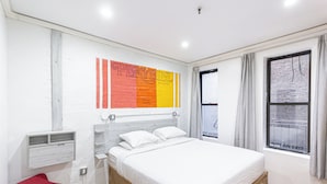 A modern bedroom with a bed, a red chair, a white wall with a Playbill Magazine poster, a window with curtains, and a sign stating "NOT AN EXIT".