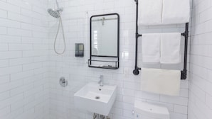 A bathroom with white tiled walls, a white sink, a mirror, a towel rack, and a showerhead.