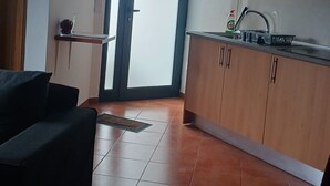 Eine moderne Küche mit Holzausstattung, einer schwarzen Arbeitsplatte und einem Edelstahl-Spülbecken. An der Wand hängt eine Uhr und eine Tür führt nach draußen.