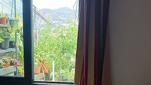 Ein Zimmer mit einem Bett, einem Vorhangfenster und Blick auf Grünflächen und Hügel.