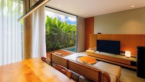 Un salon moderne avec une table à manger en bois, des sièges confortables, un téléviseur à écran plat et une grande fenêtre donnant sur un jardin.