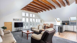 Ein großzügiges Lofts mit hohen Decken, freiliegenden Holzbalken, einer gemütlichen Sitzecke mit Ledersofas, einem Flachbildfernseher und einer Küche mit großem Fenster.