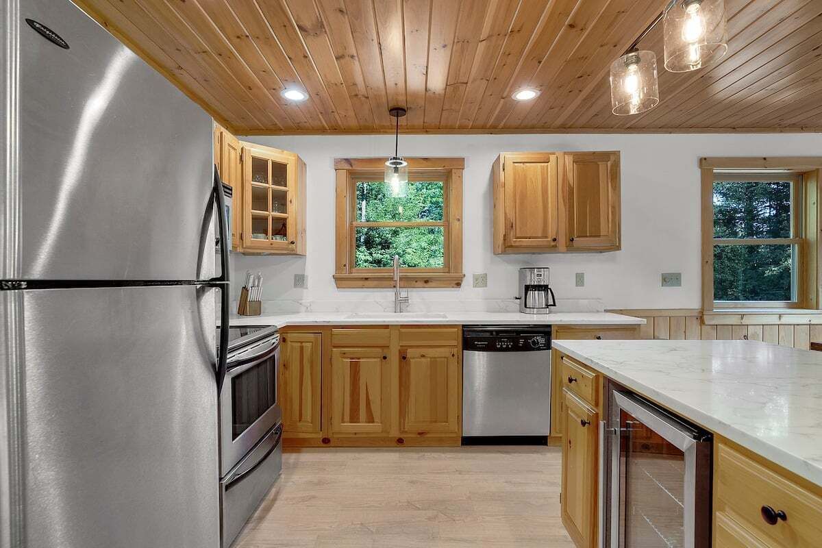Eine moderne Küche mit Holzschränken, Edelstahlgeräten und einem großen Fenster, das natürliches Licht hereinlässt.