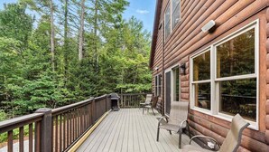 A wooden deck with chairs and a grill, surrounded by forest. - Bethel Hillside Chalet: Hot Tub + Fire Pit (Bethel)