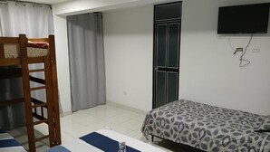 Une chambre avec un lit superposé, un lit simple, un téléviseur fixé au mur et une porte.