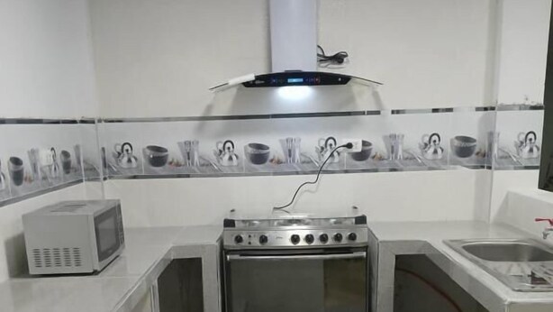 Une cuisine compacte dotée d’un four encastré, d’un four à micro-ondes et d’une hotte de cuisine en acier inoxydable.