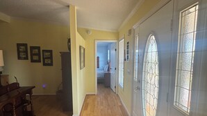 Un couloir avec un plancher en bois, un coin repas avec une table et des chaises, et une porte dotée d’une fenêtre en verre.