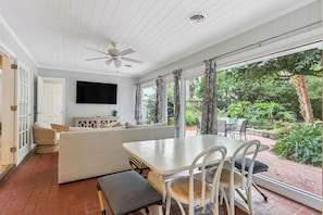A room with a ceiling fan, a flat-screen TV, a sofa, and a dining table with chairs.