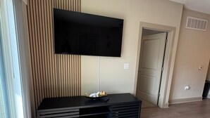 Una sala de estar moderna con un televisor de pantalla plana montado en la pared, un mueble de entretenimiento negro y un ventanal corredizo que da a un balcón.