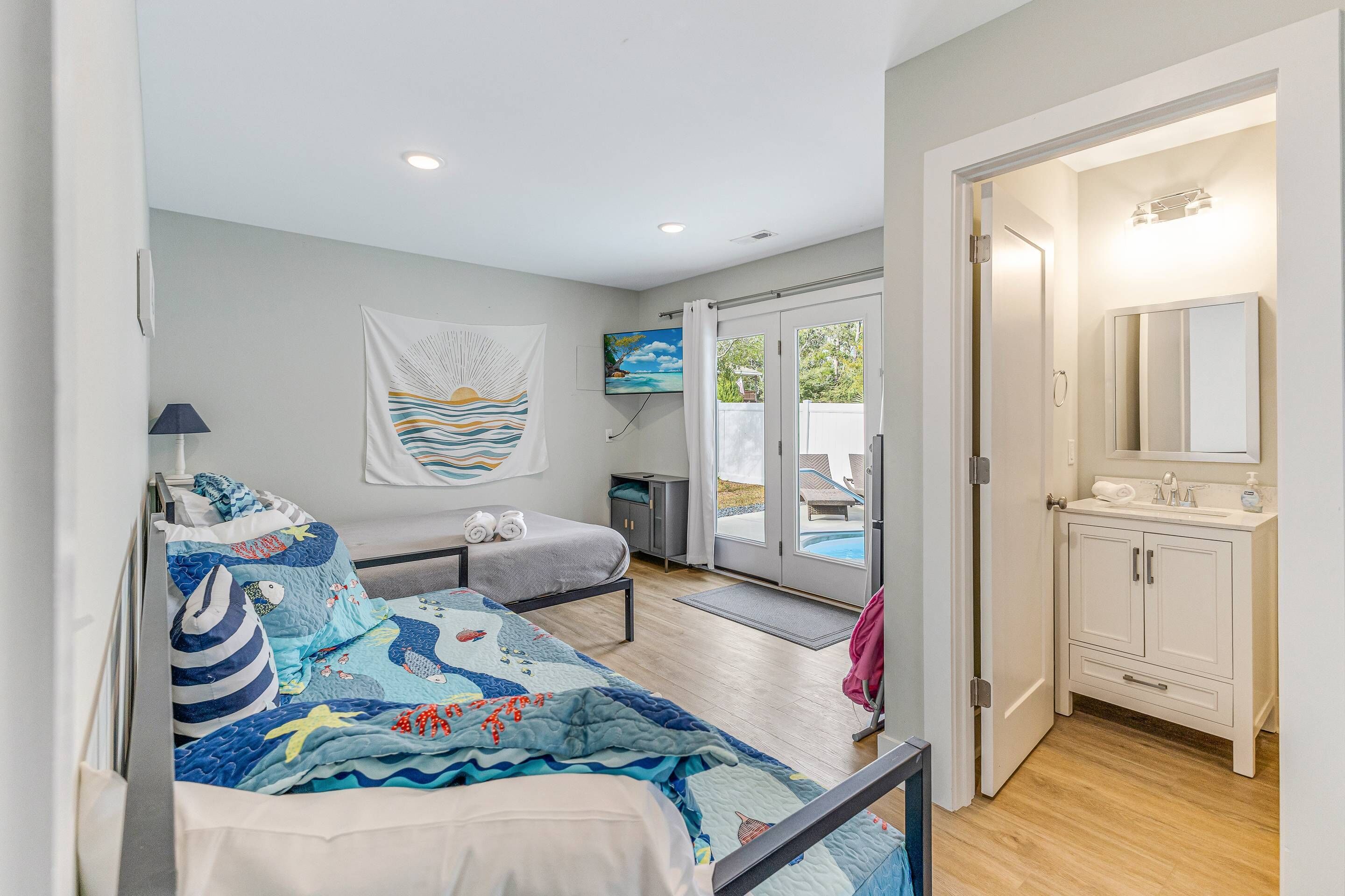 A bedroom with a bed, a bedside table, a TV, a painting, and a bathroom with a sink and mirror.