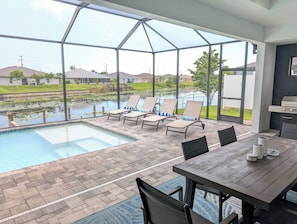Uma área na piscina com espreguiçadeiras, uma mesa e uma churrasqueira.