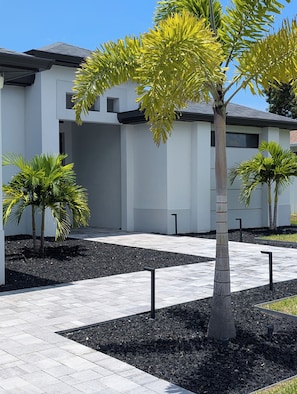 Un edificio moderno con un sendero pavimentado y pequeñas palmeras.