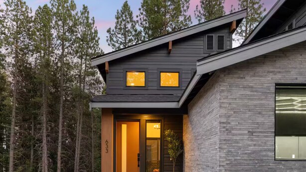 Una casa moderna con techo oscuro, ventanas grandes y el número 633 en la puerta.