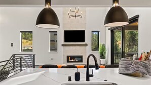 Una cocina moderna con una isla grande, una chimenea y un área de comedor con cojines naranja.