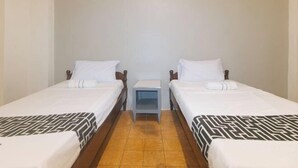 A room with two single beds, a small bedside table, and a plain wall.